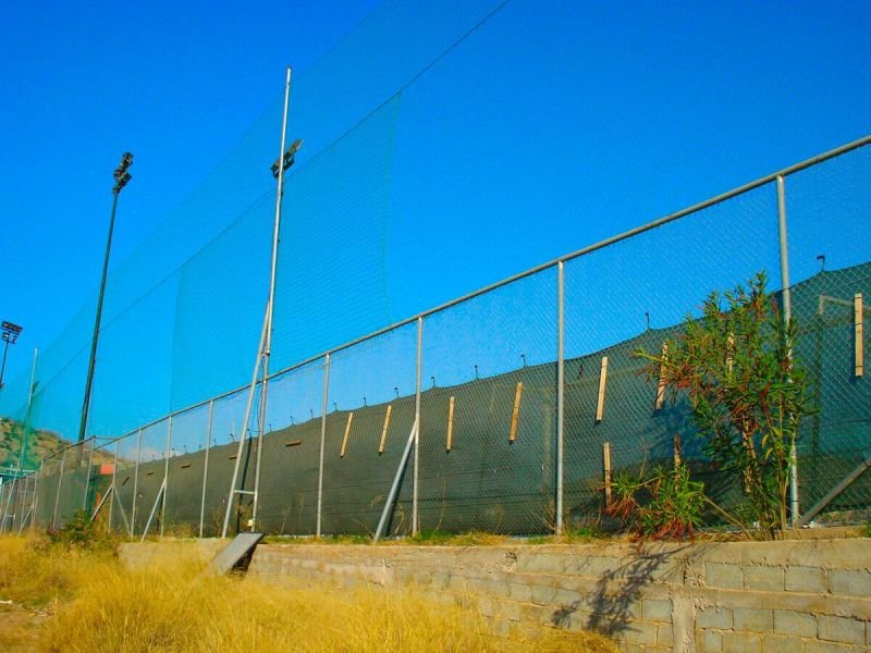 Περίφραξη γηπέδου με μεταλλικούς στύλους, συρματόπλεγμα, τσιμεντένια βάση και ανθεκτικά υλικά κατάλληλα για αθλητικές χρήσεις.