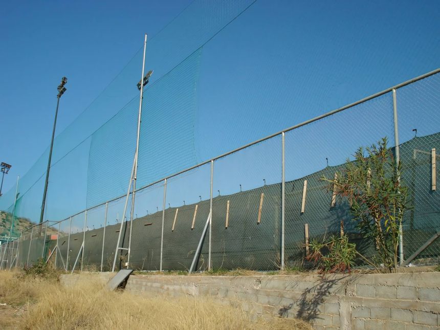 Περίφραξη γηπέδου με μεταλλικούς στύλους, συρματόπλεγμα, τσιμεντένια βάση και ανθεκτικά υλικά κατάλληλα για αθλητικές χρήσεις.