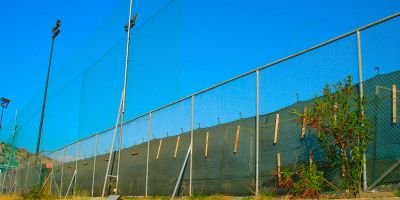 Περίφραξη γηπέδου με μεταλλικούς στύλους, συρματόπλεγμα, τσιμεντένια βάση και ανθεκτικά υλικά κατάλληλα για αθλητικές χρήσεις.